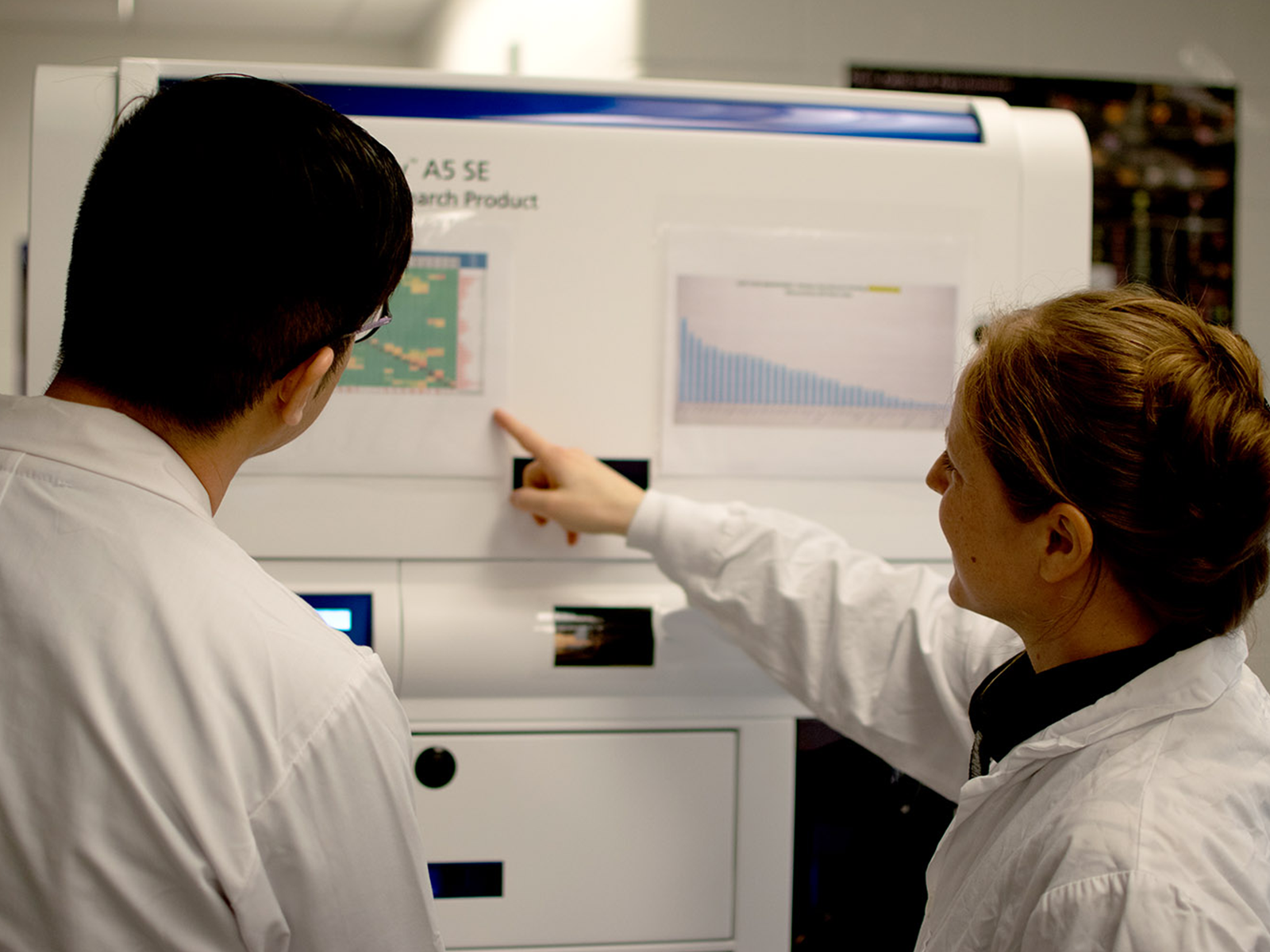 Two people in lab coats pointing at poster on a research cell sorter.