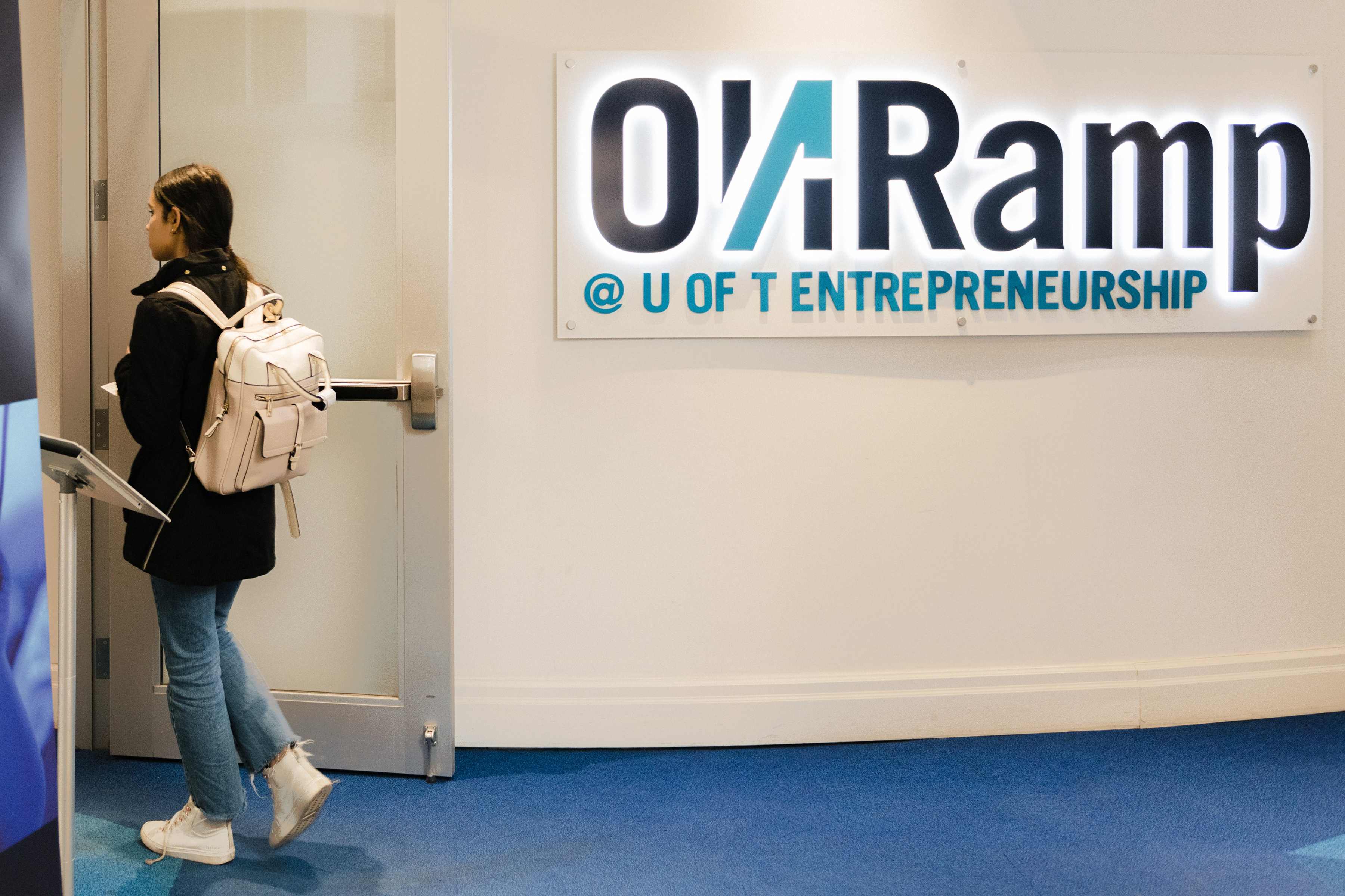 A woman exiting a room near a sign that says "ONRamp @ U of T Entrepreneurship".