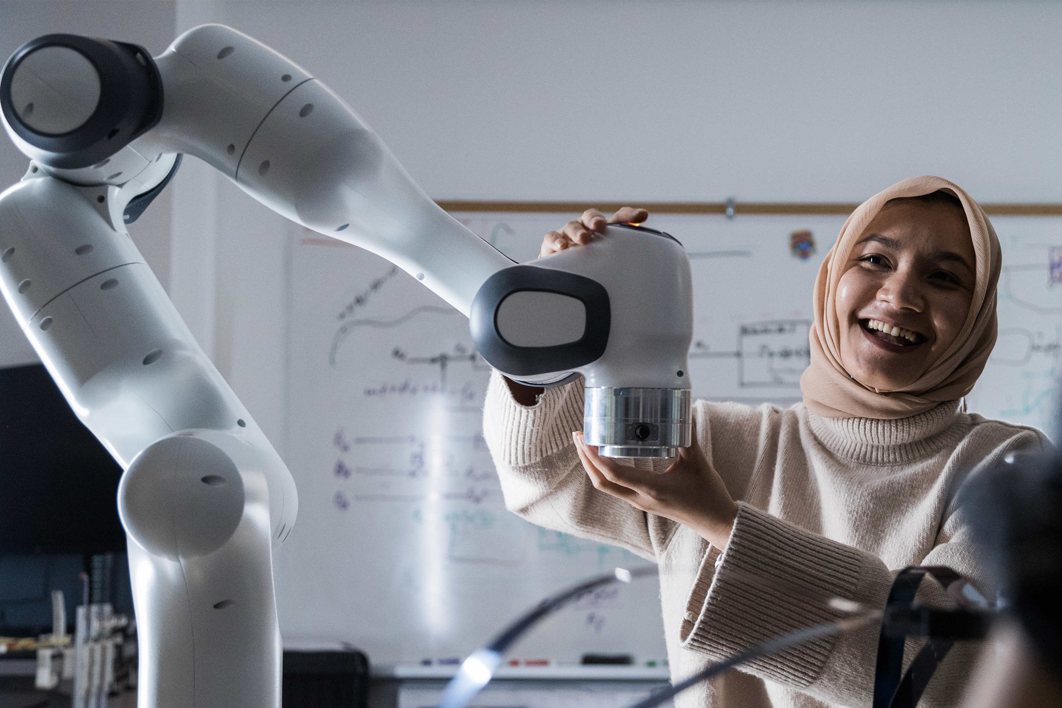 A woman working with a robotic arm in a classrooms setting.